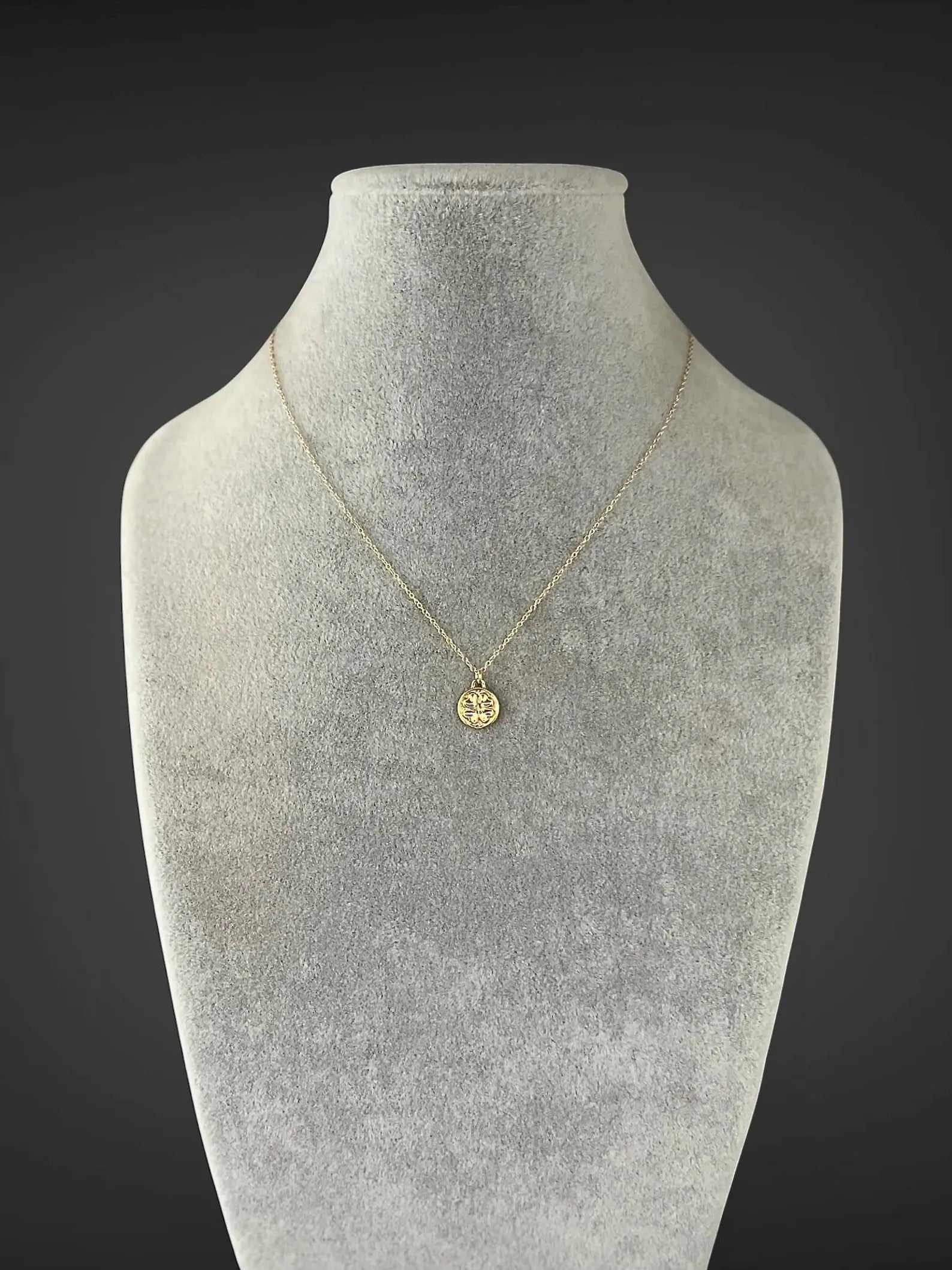 Gold necklace with a pendant on a gray mannequin bust against a dark background