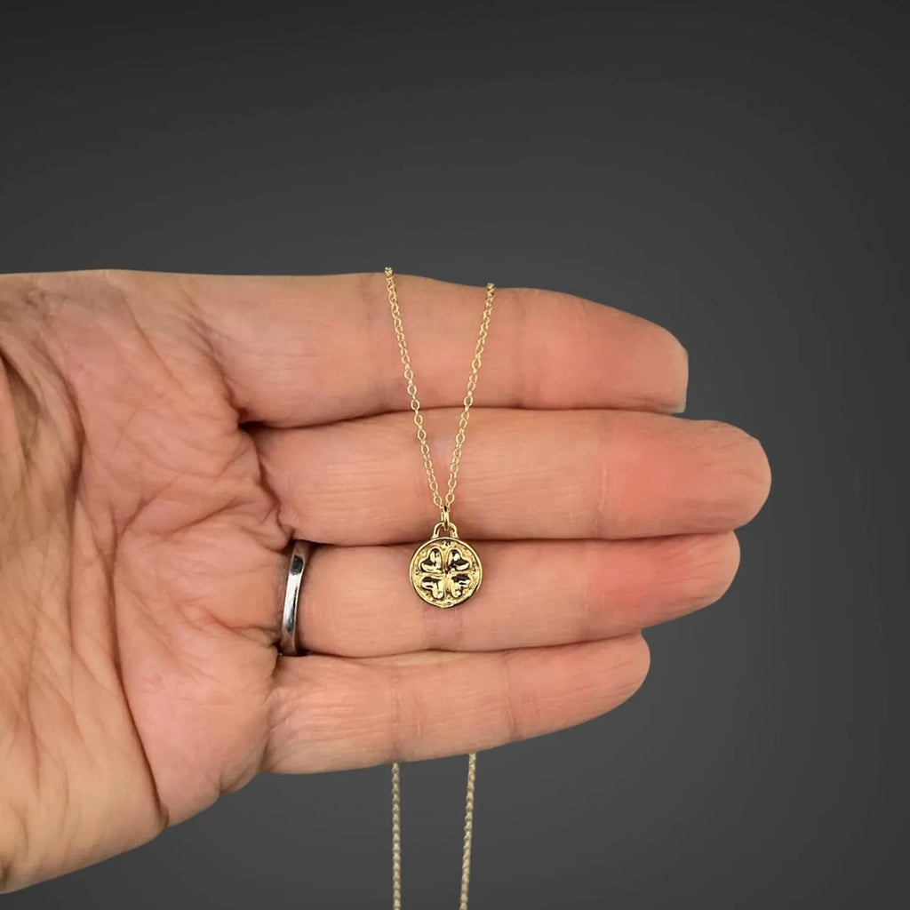 Gold necklace with a pendant held in a hand against a dark background