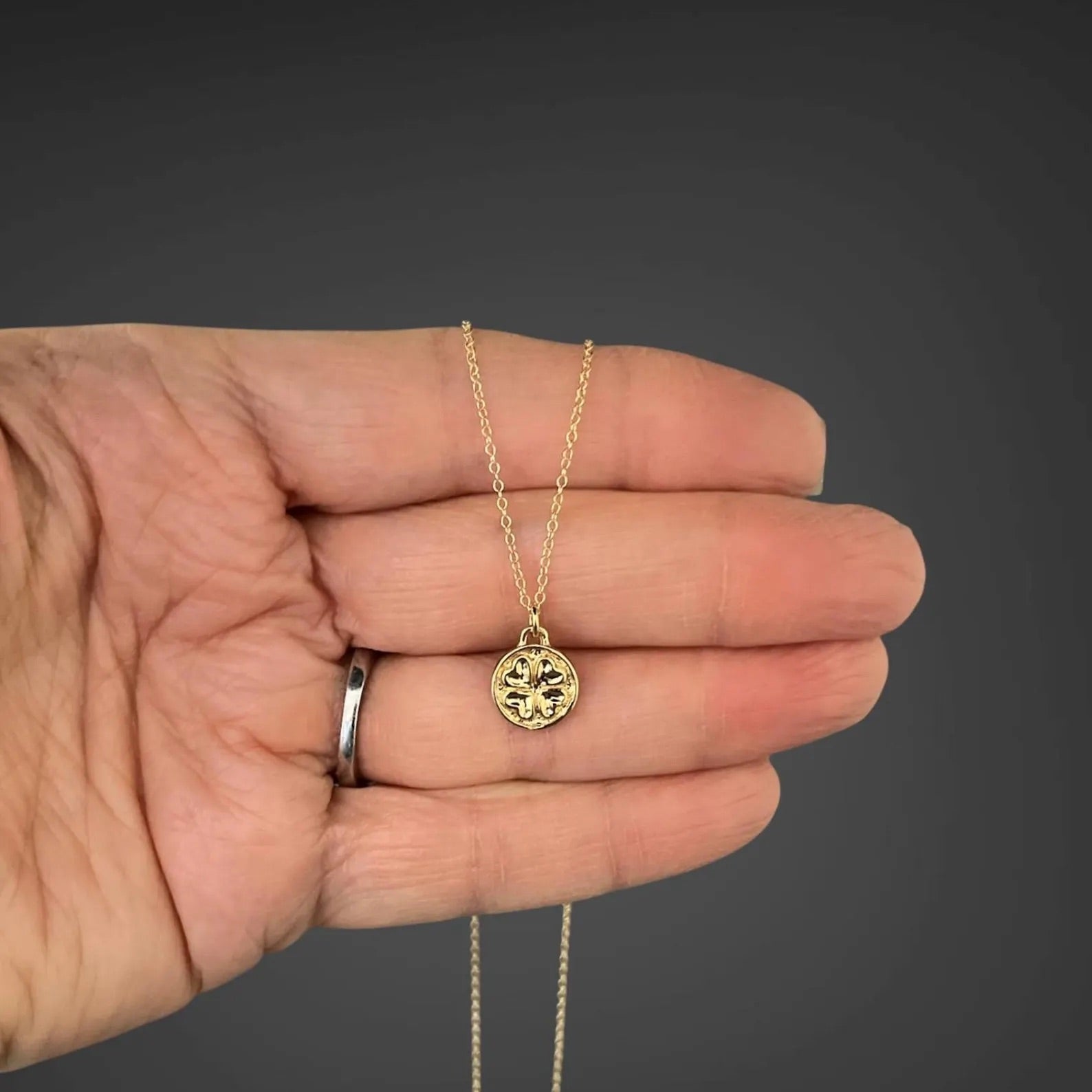 Gold necklace with a pendant held in a hand against a dark background