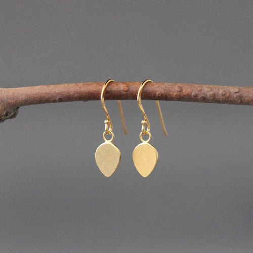 Gold teardrop earrings hanging on a branch against a gray background