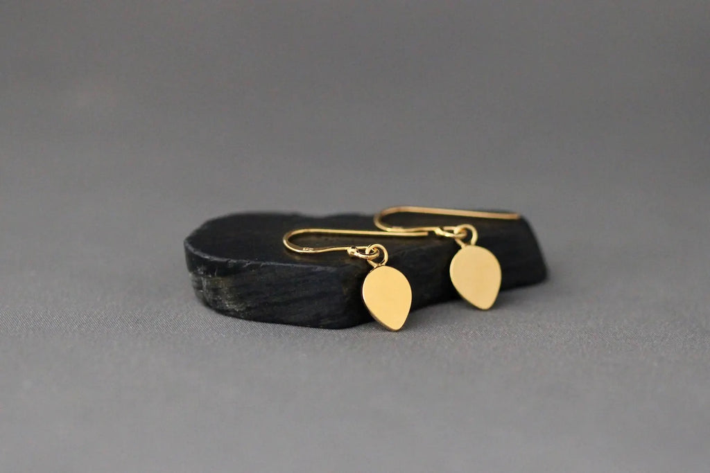 Gold earrings on a black stand against a gray background
