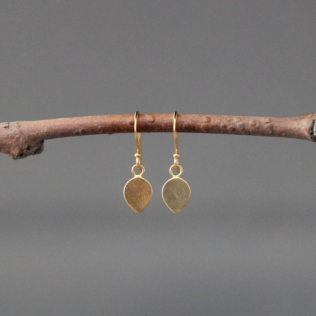 Gold earrings hanging from a branch against a gray background