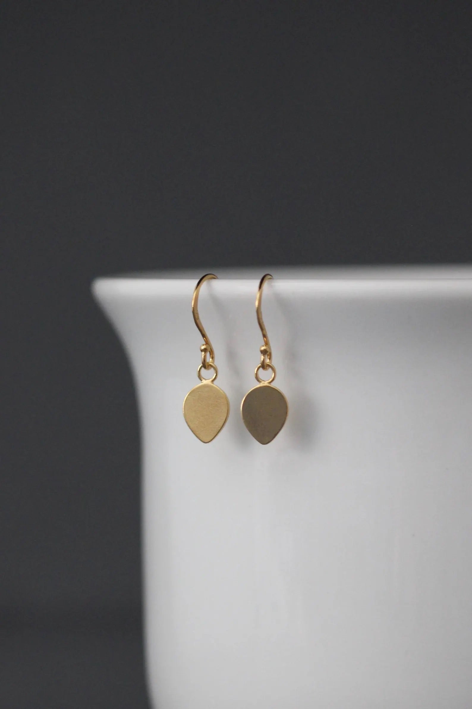 Gold earrings with leaf-shaped drops on a white stand against a dark background