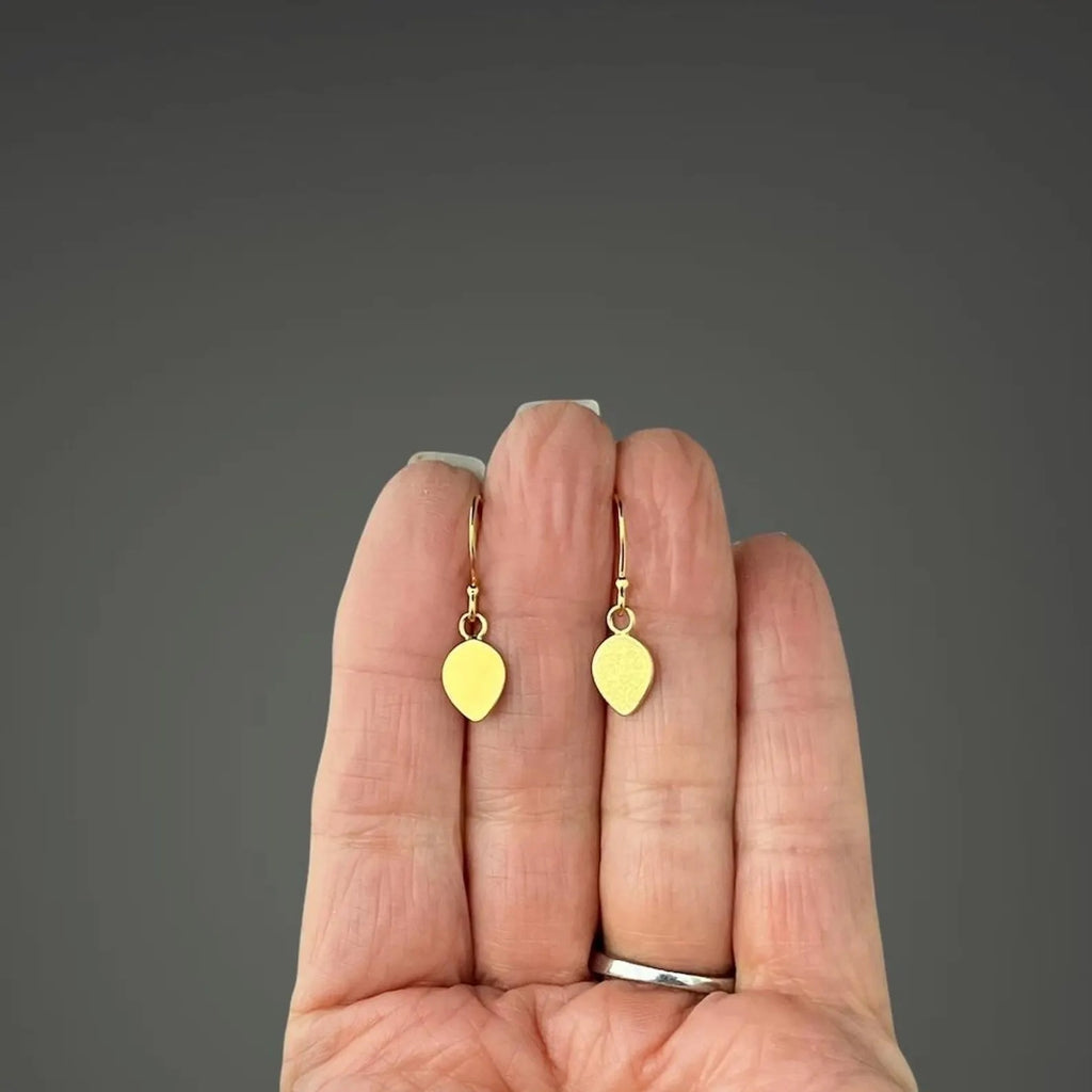 Gold earrings held between fingers against a gray background
