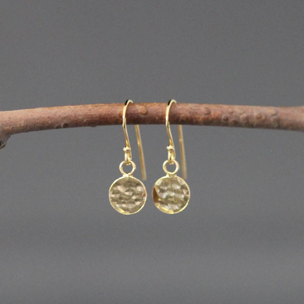 Gold earrings hanging from a branch against a gray background