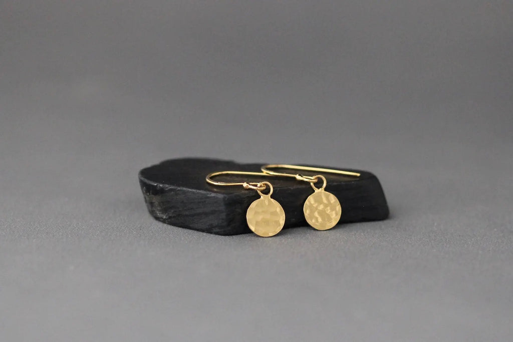 Gold earrings on a black stand against a gray background