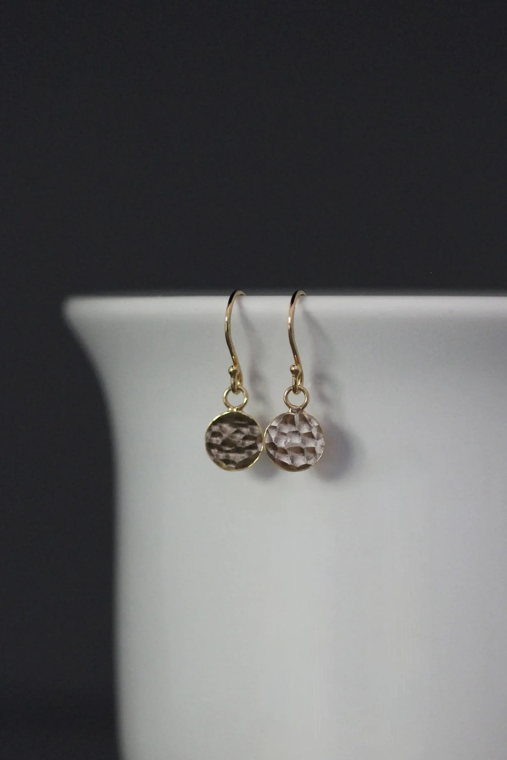 Pair of earrings with round dangling charms on a white stand against a dark background