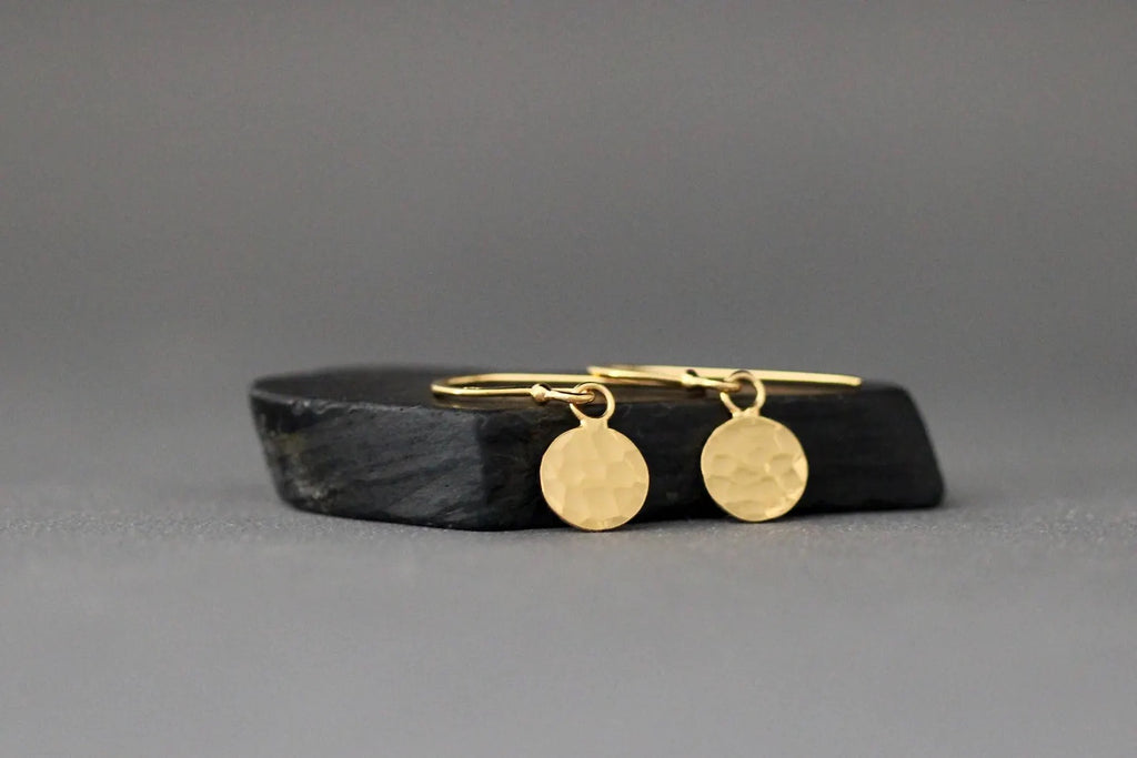 Gold hoop earrings with round pendants on a black stone surface against a gray background