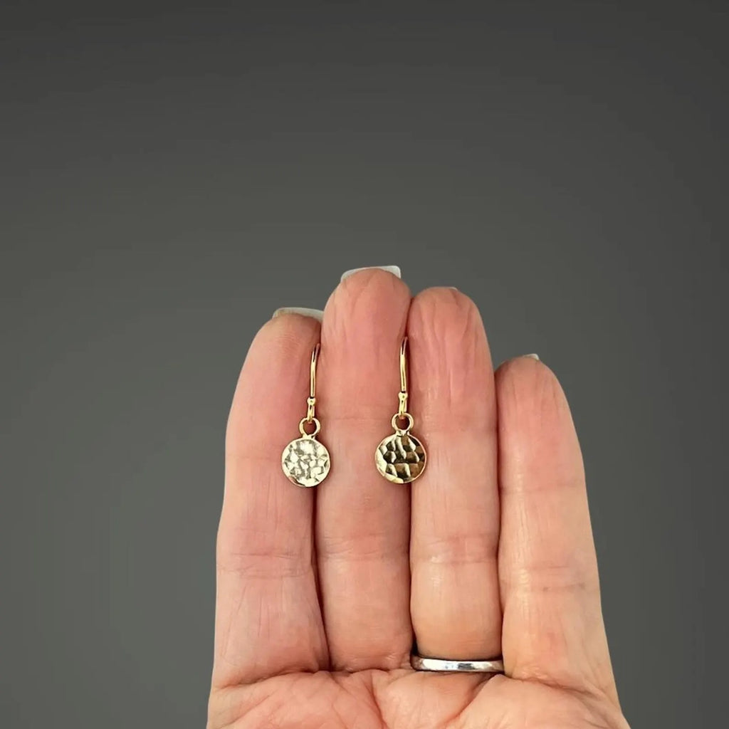 Gold earrings held in a hand against a gray background