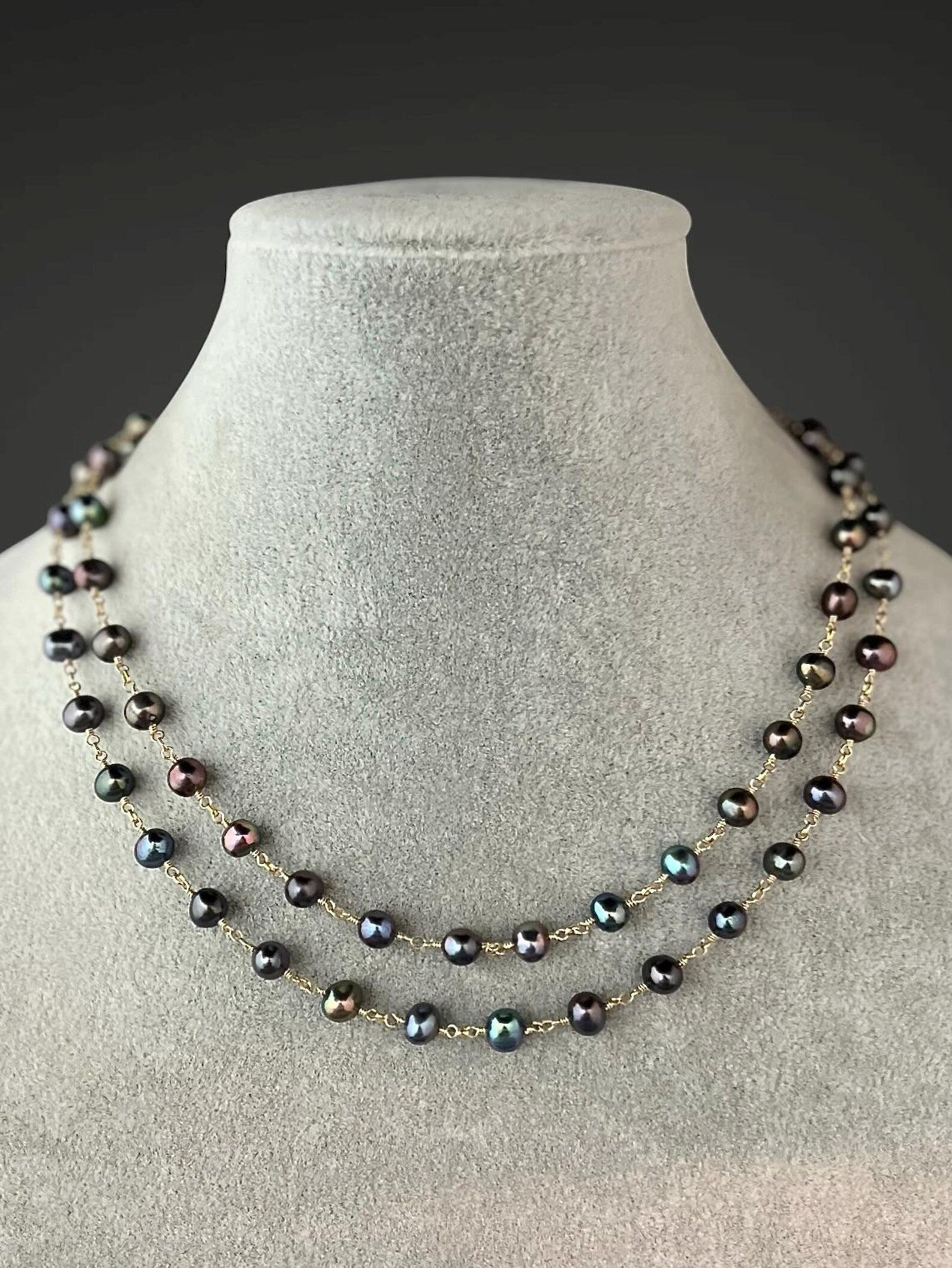 Layered dark freshwater pearl necklace with gold connectors, draped on bust form.