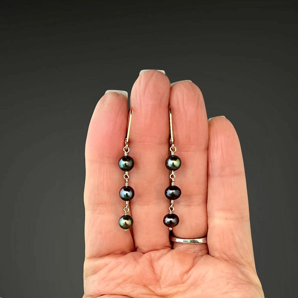 Gold wire-wrapped earrings with dark freshwater pearl drops, three-bead design.