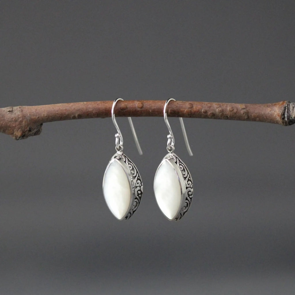 White mother of pearl and silver pendant earrings against a gray backdrop