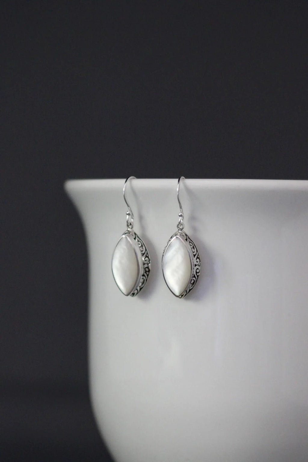 White mother of pearl and silver pendant earrings against a gray backdrop