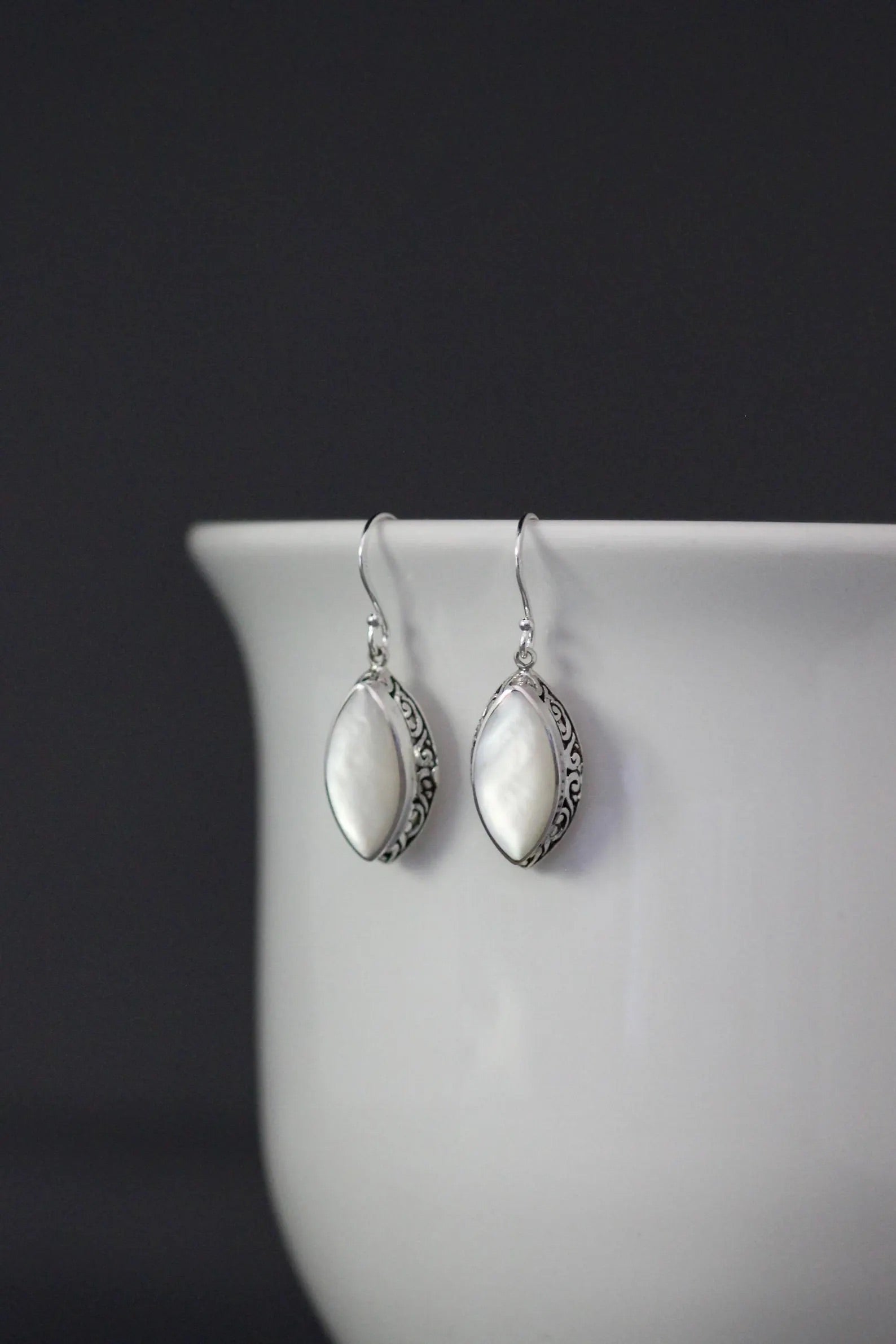 White mother of pearl and silver pendant earrings against a gray backdrop