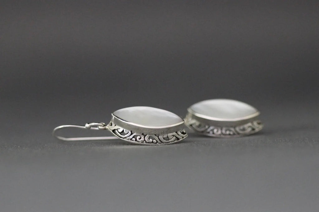 White mother of pearl and silver pendant earrings against a gray backdrop