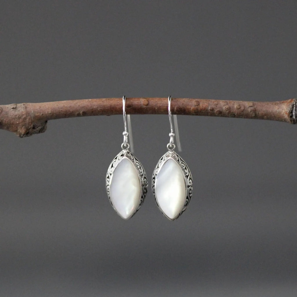 White mother of pearl and silver pendant earrings against a gray backdrop