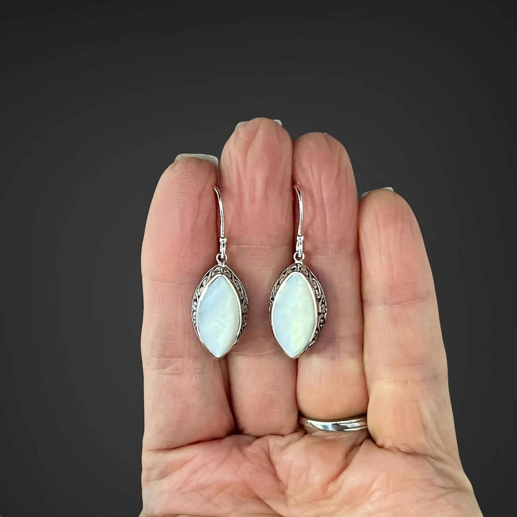 White mother of pearl and silver pendant earrings held in the palm of a person's hand