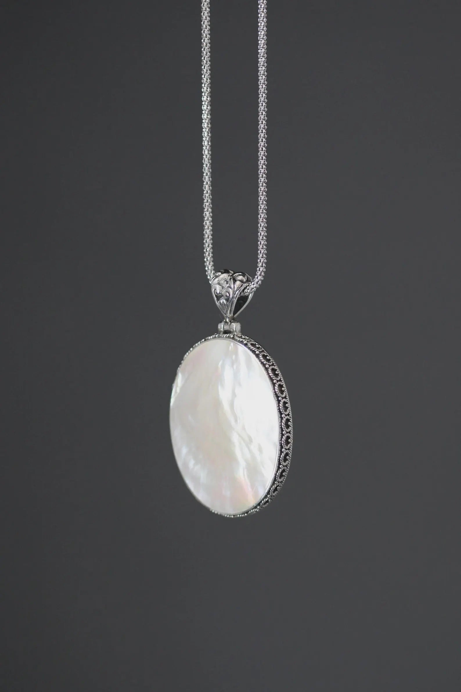Close up profile of a white mother of pearl and silver pendant necklace
