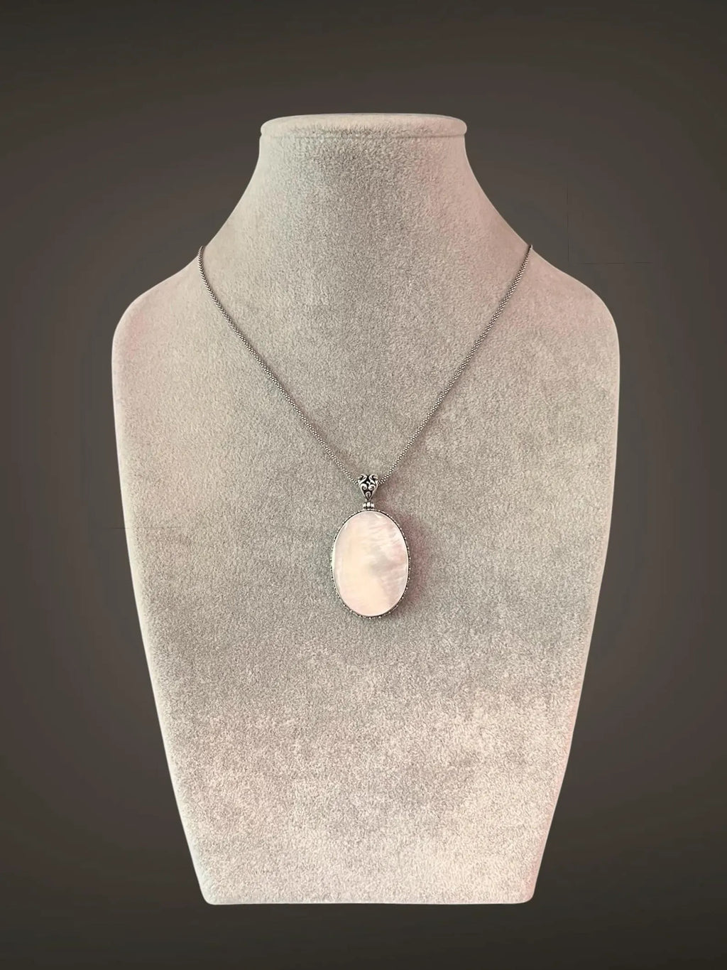 A white mother of pearl and silver pendant necklace displayed on a gray mannequin bust