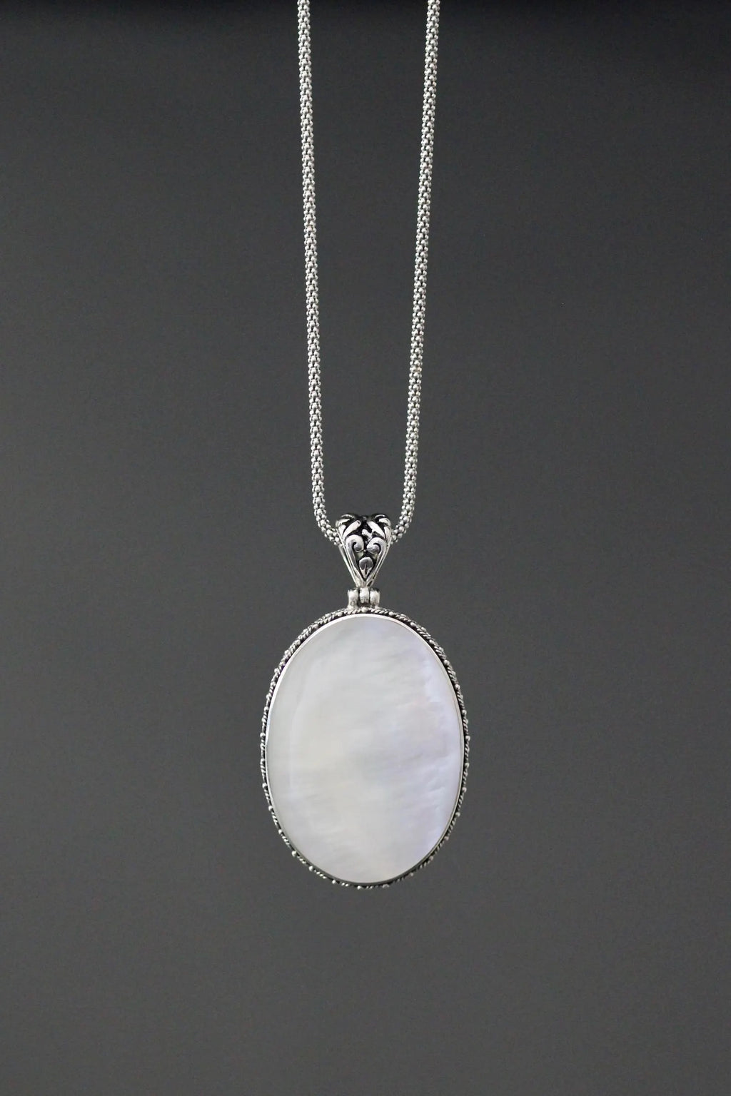 Close up image of a white mother of pearl and silver pendant necklace against a gray backdrop