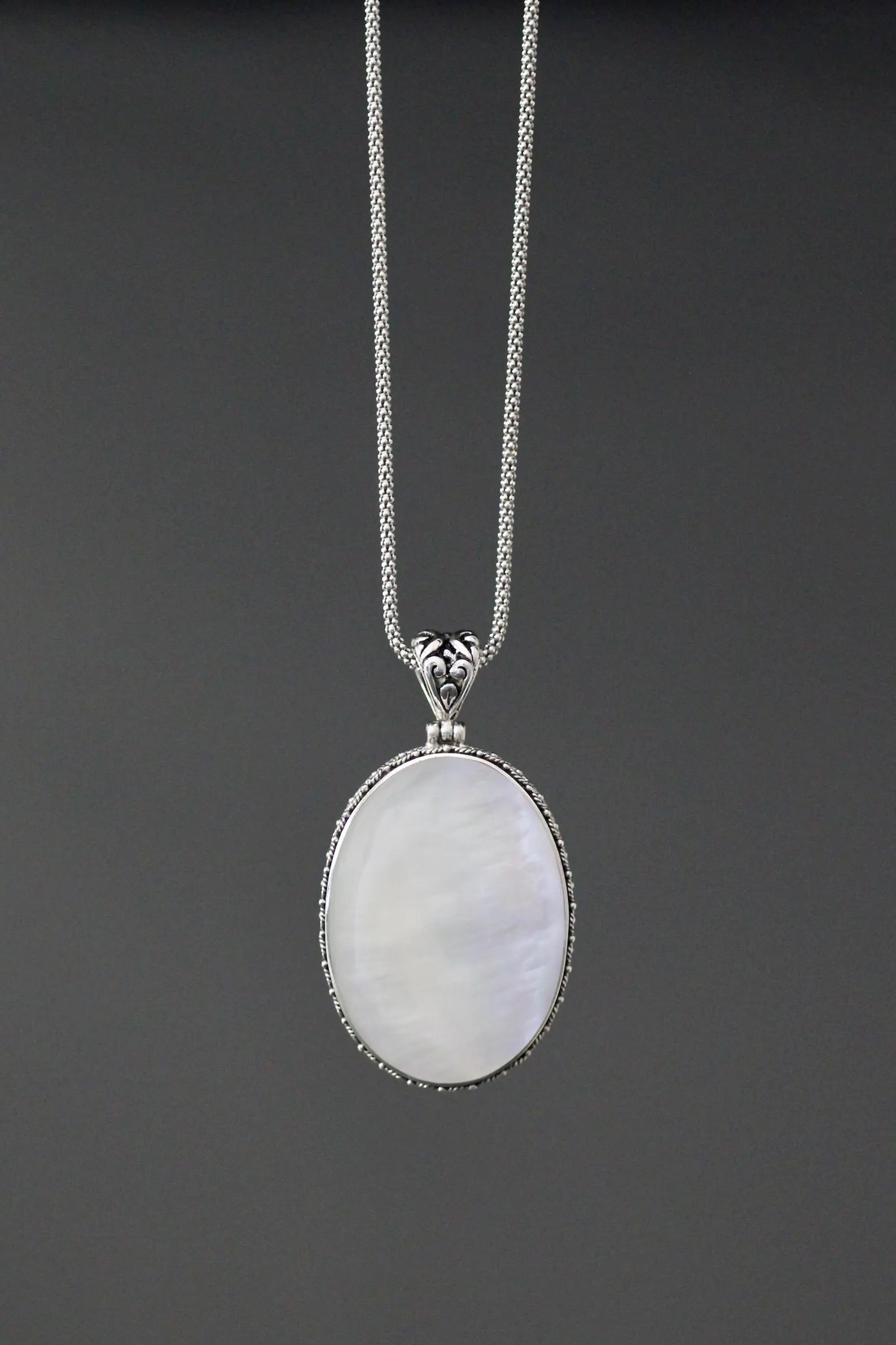 Close up image of a white mother of pearl and silver pendant necklace against a gray backdrop