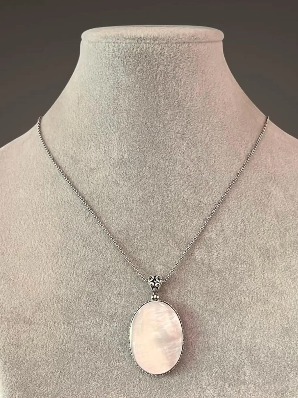A white mother of pearl and silver pendant necklace displayed on a gray mannequin bust