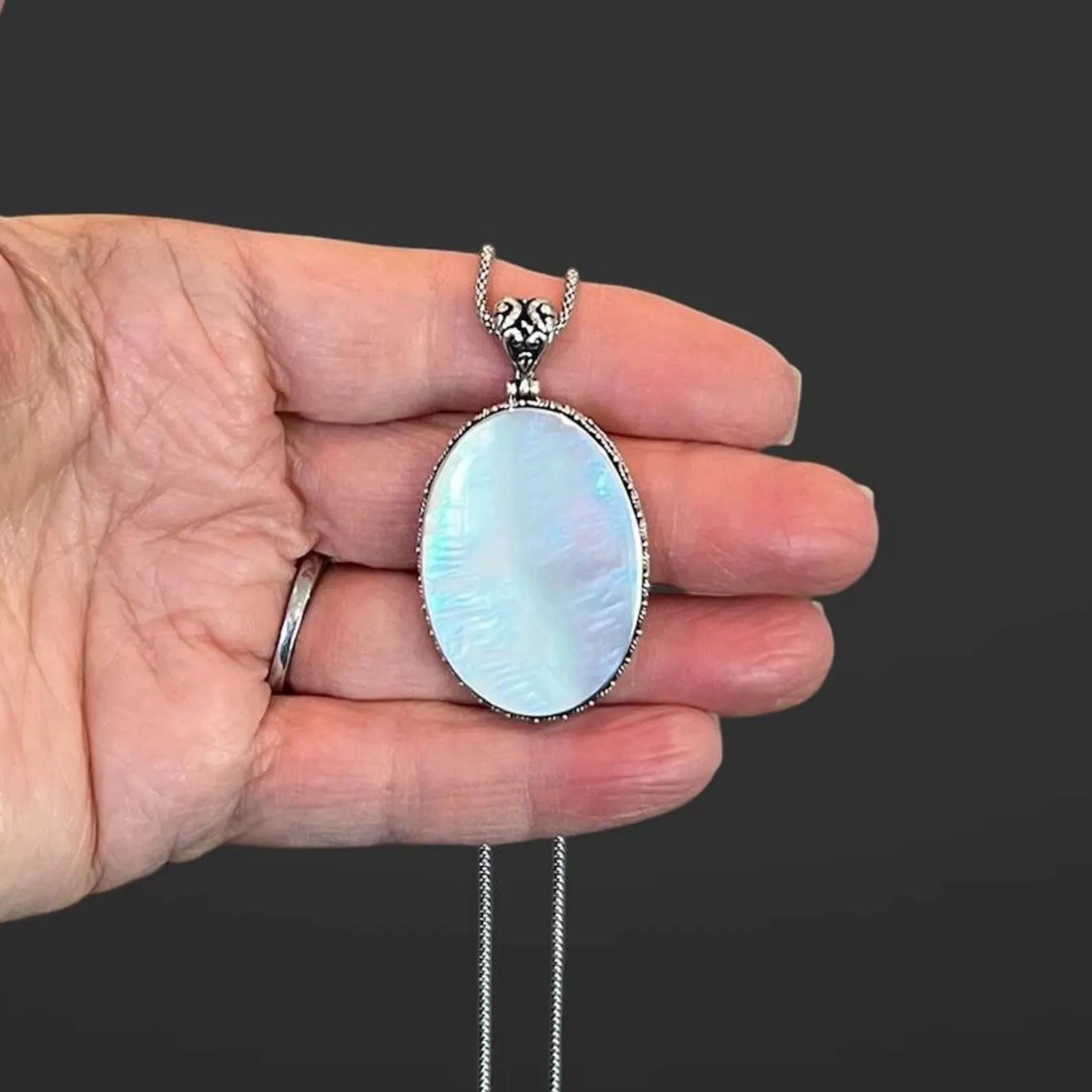 A white mother of pearl and silver pendant necklace displayed against the palm of a person's hand