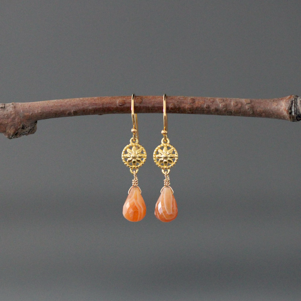 Gold earrings with orange teardrop stones on a branch against a gray background