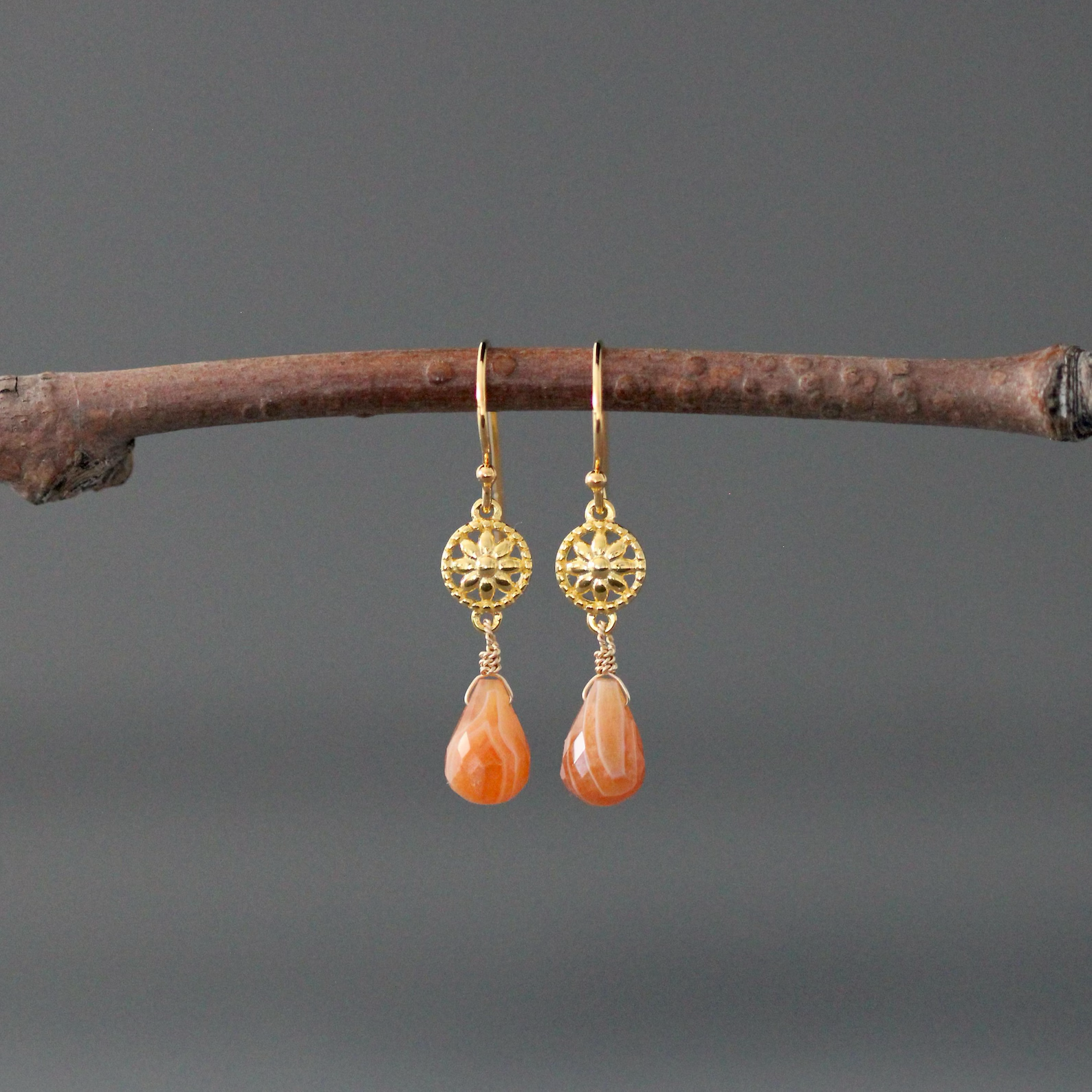 Gold earrings with orange teardrop stones on a branch against a gray background