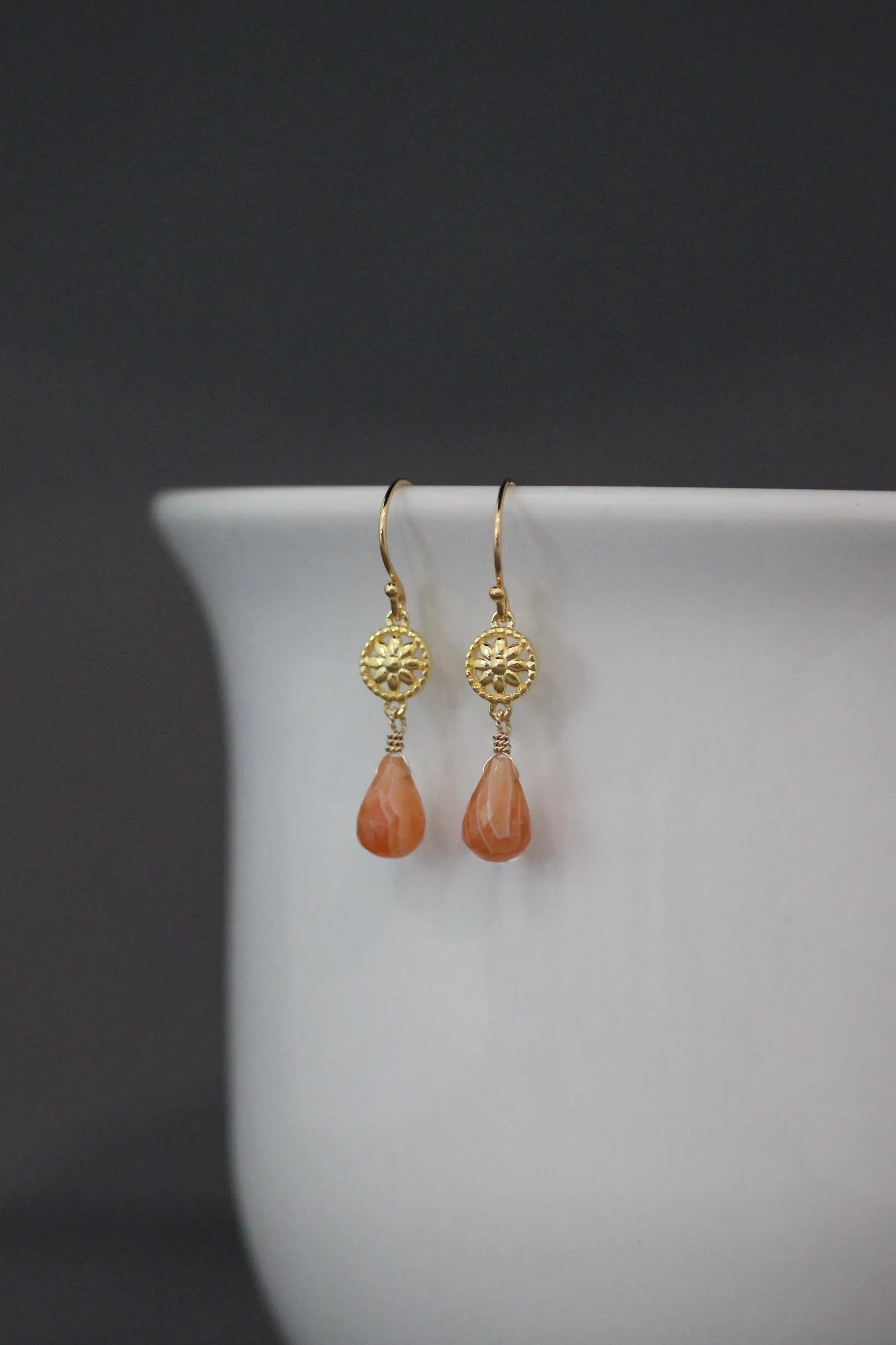 Gold earrings with orange teardrop beads on a white surface with a dark background