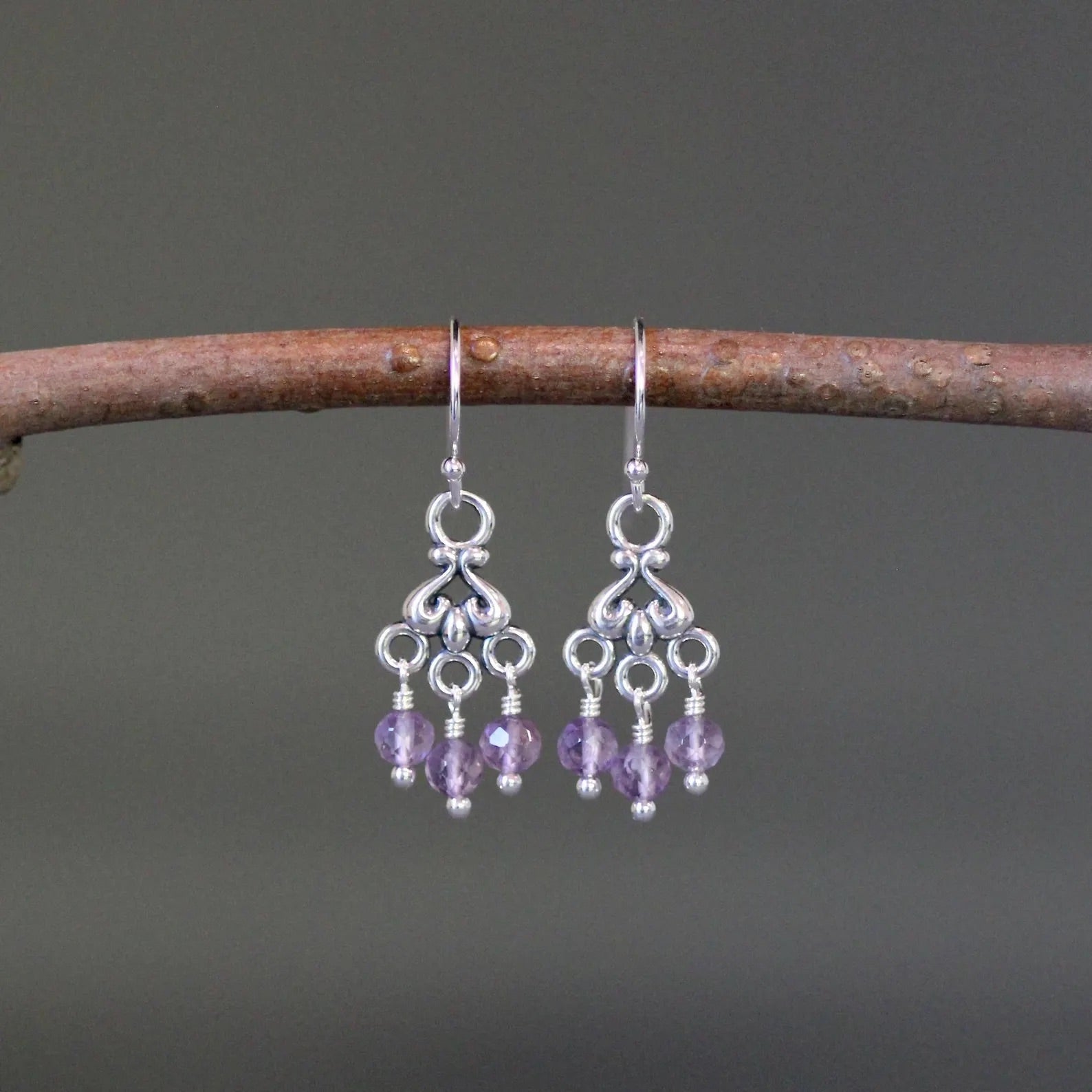 Purple amethyst and silver chandelier earrings against a gray backdrop