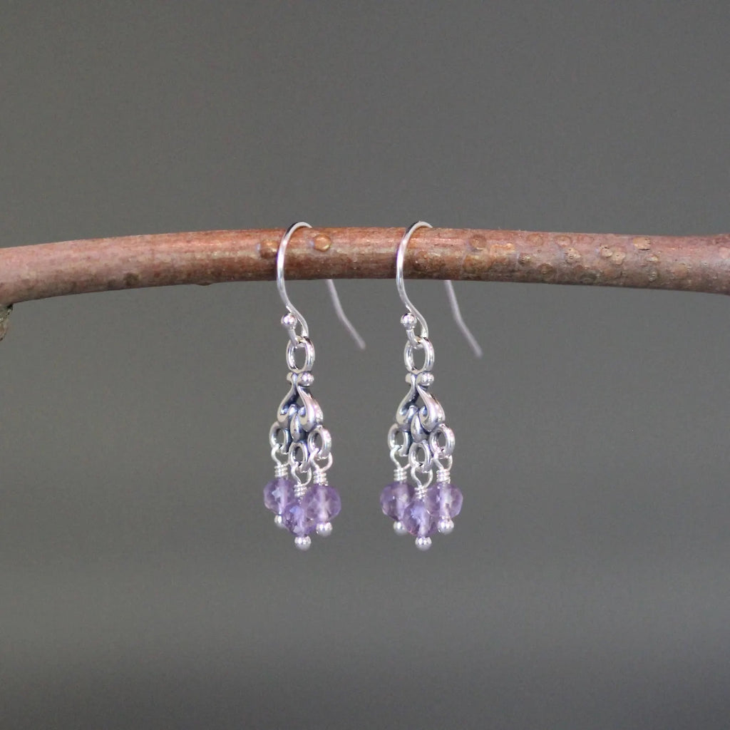 Purple amethyst and silver chandelier earrings against a gray backdrop