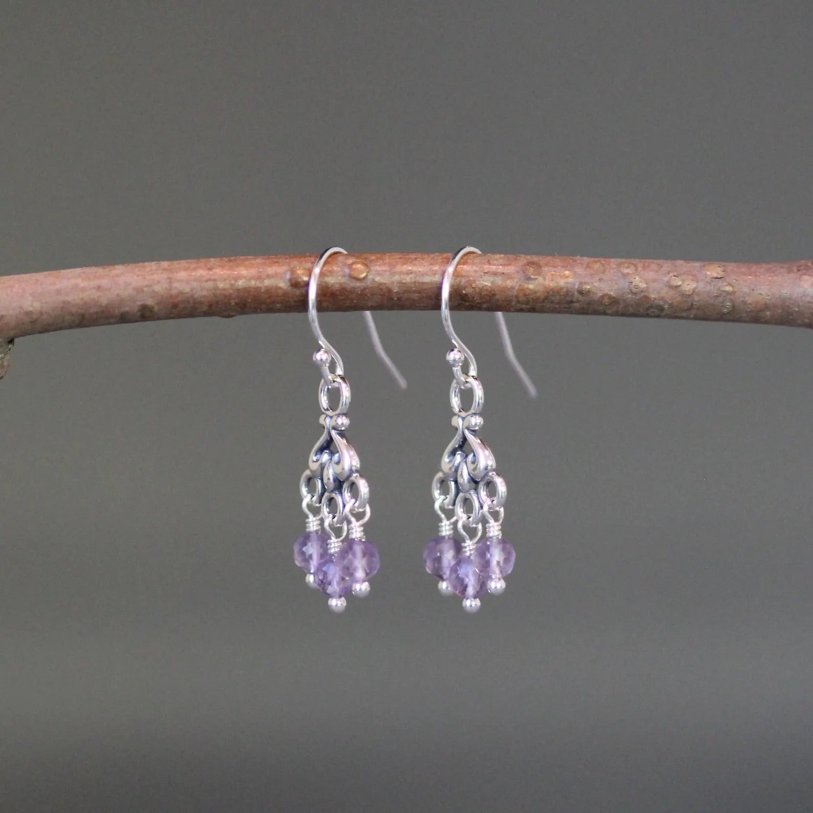Purple amethyst and silver chandelier earrings against a gray backdrop