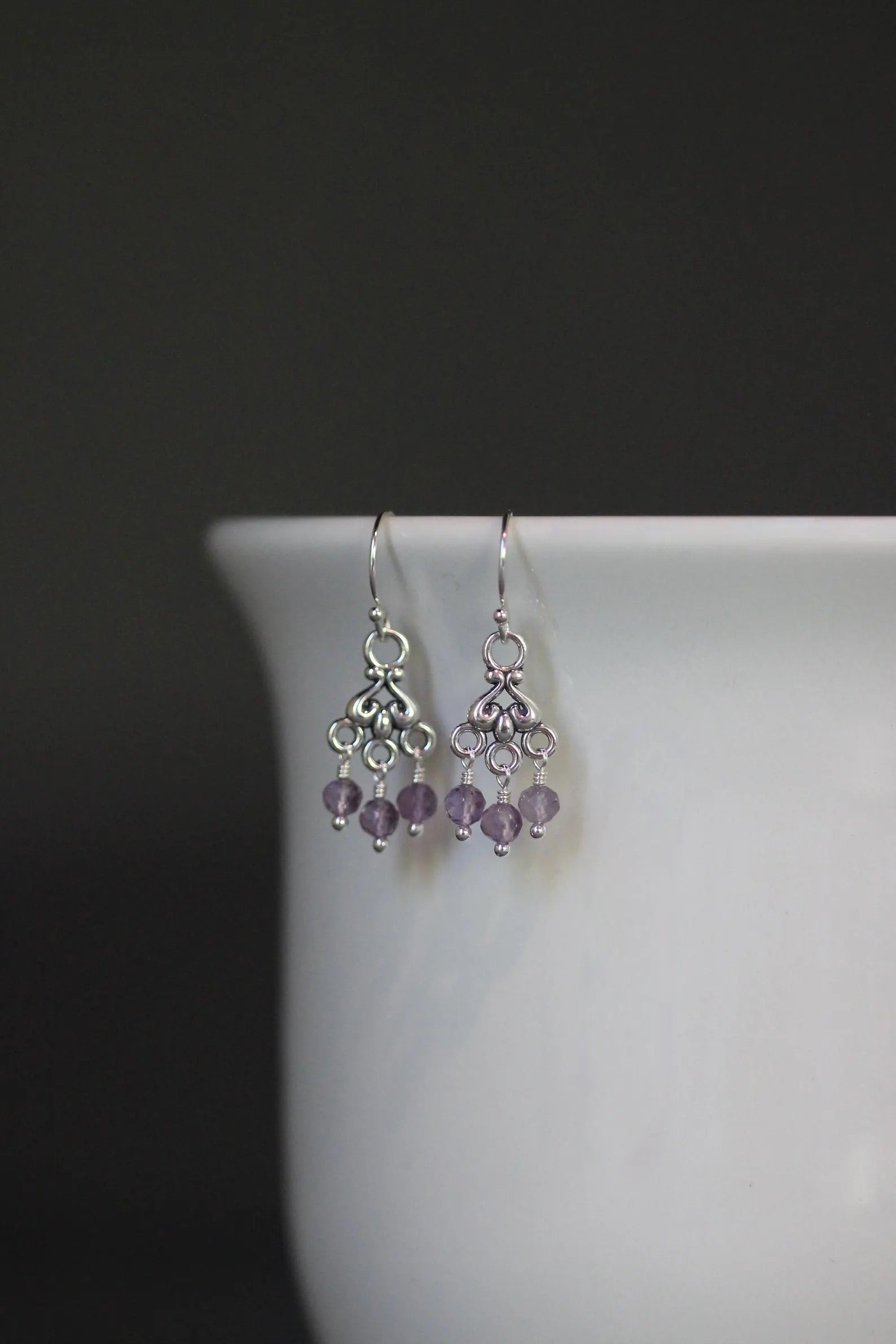 Purple amethyst and silver chandelier earrings against a gray backdrop