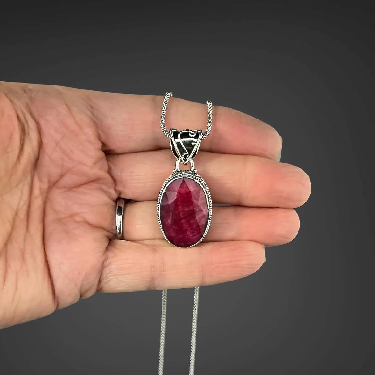 Sterling silver ruby-red oval pendant on chain held in hand