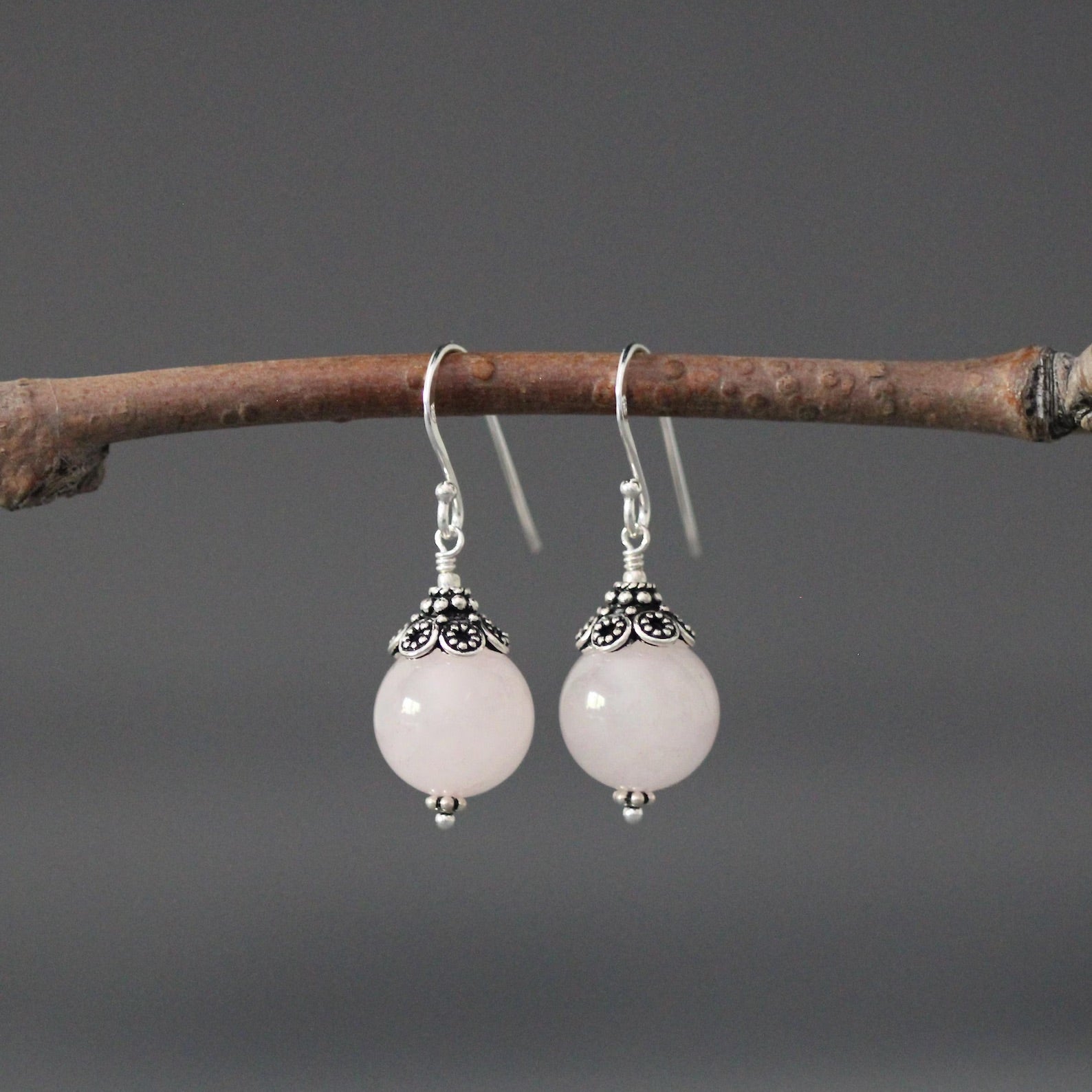 Rose quartz and silver earrings against a gray backdrop