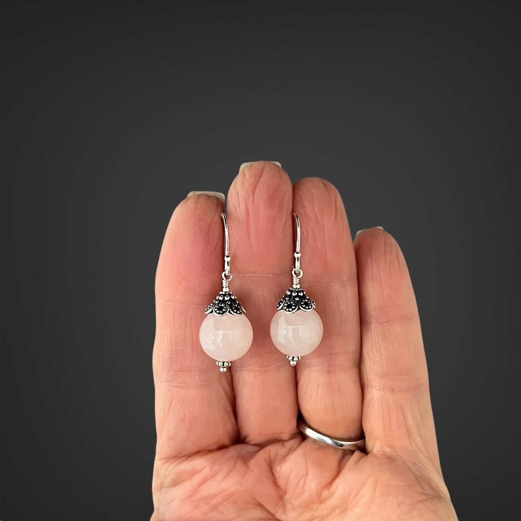 Rose quartz and silver earrings held in the palm of a person's hand
