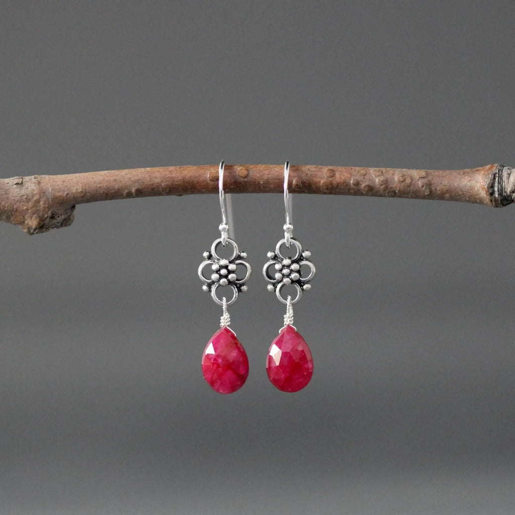Earrings with teardrop-shaped ruby stones and silver earwires against a gray backdrop