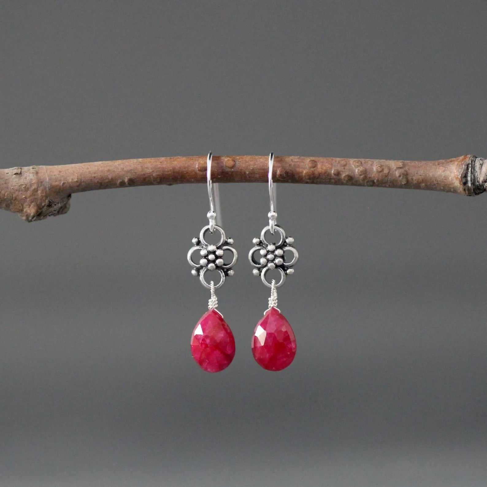 Earrings with teardrop-shaped ruby stones and silver earwires against a gray backdrop