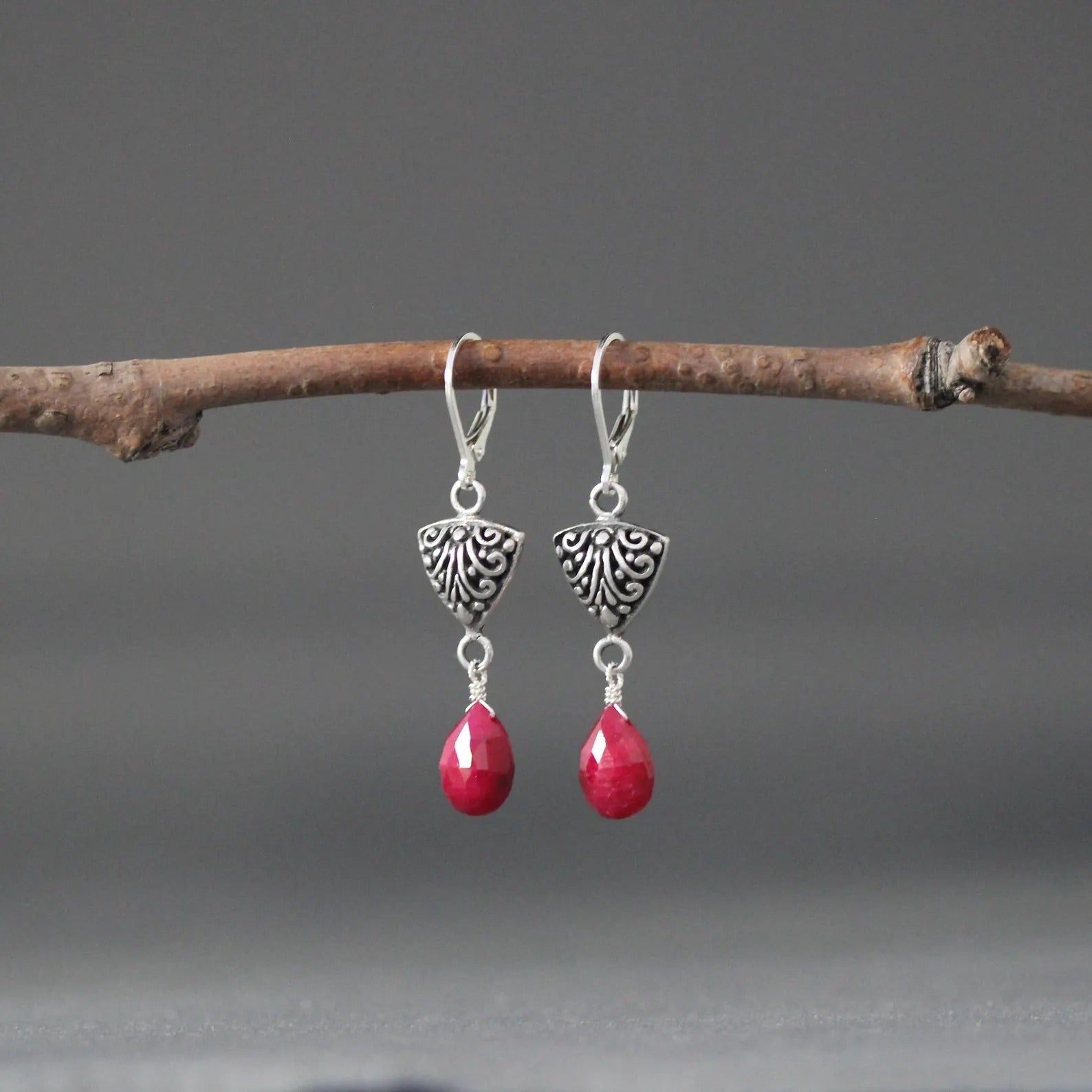 Silver Bali-style teardrop earrings with detailed caps and red teardrop gemstones