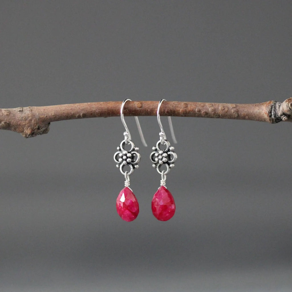 Earrings with teardrop-shaped ruby stones and silver earwires against a gray backdrop