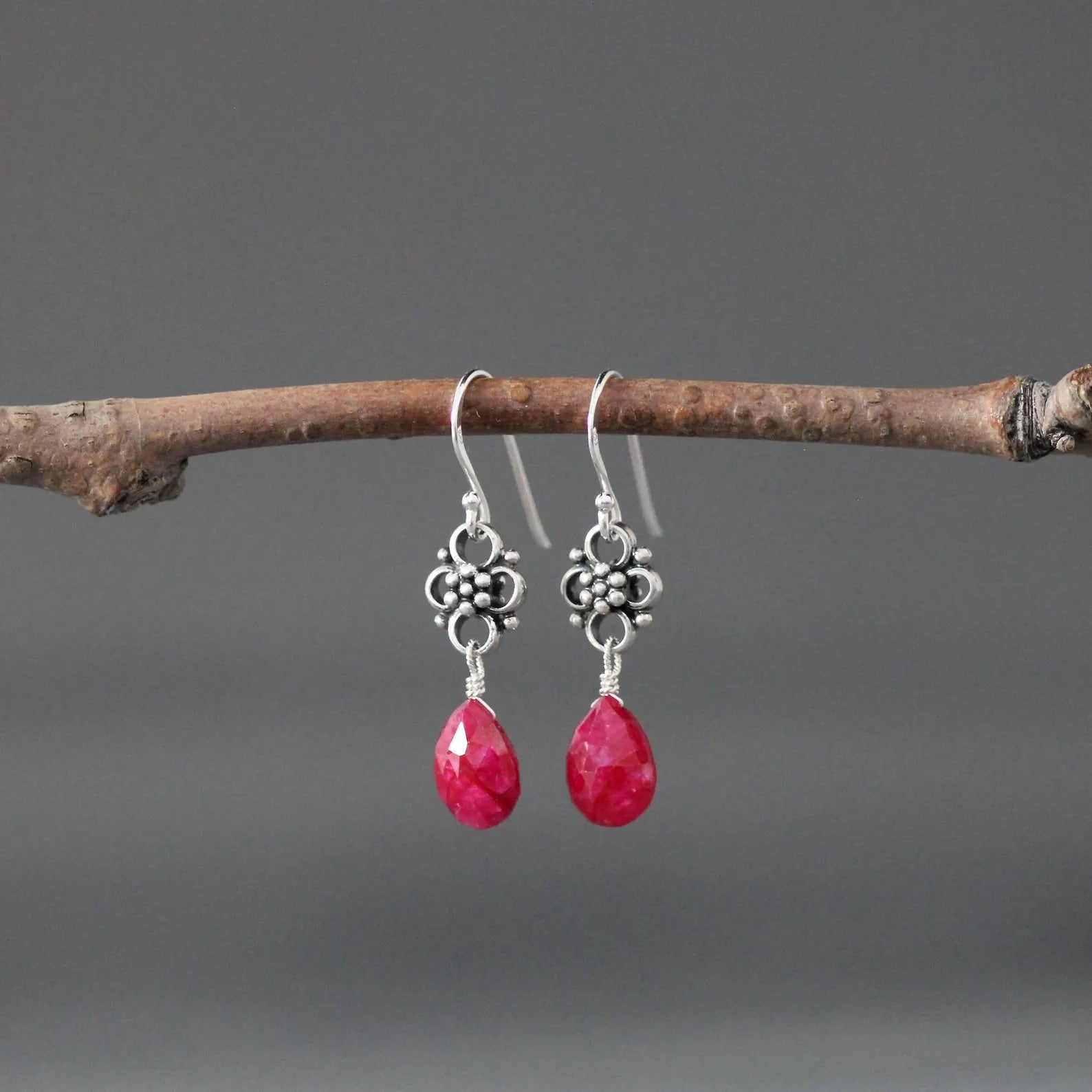 Earrings with teardrop-shaped ruby stones and silver earwires against a gray backdrop