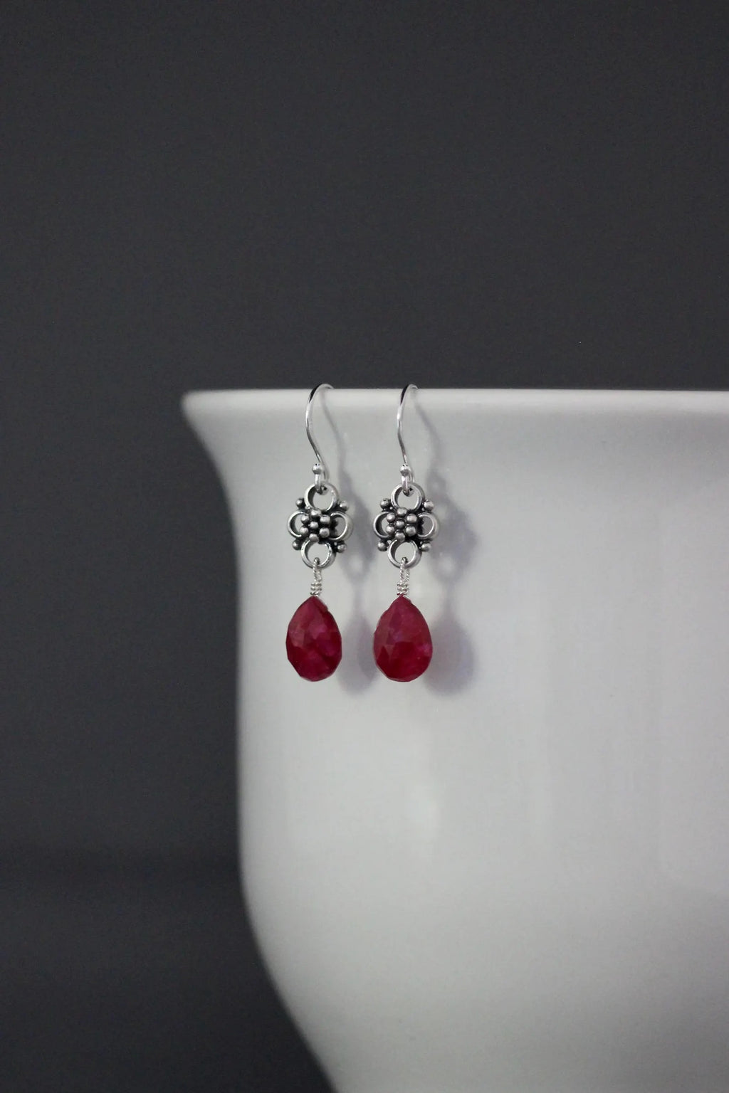 Earrings with teardrop-shaped ruby stones and silver earwires against a gray backdrop