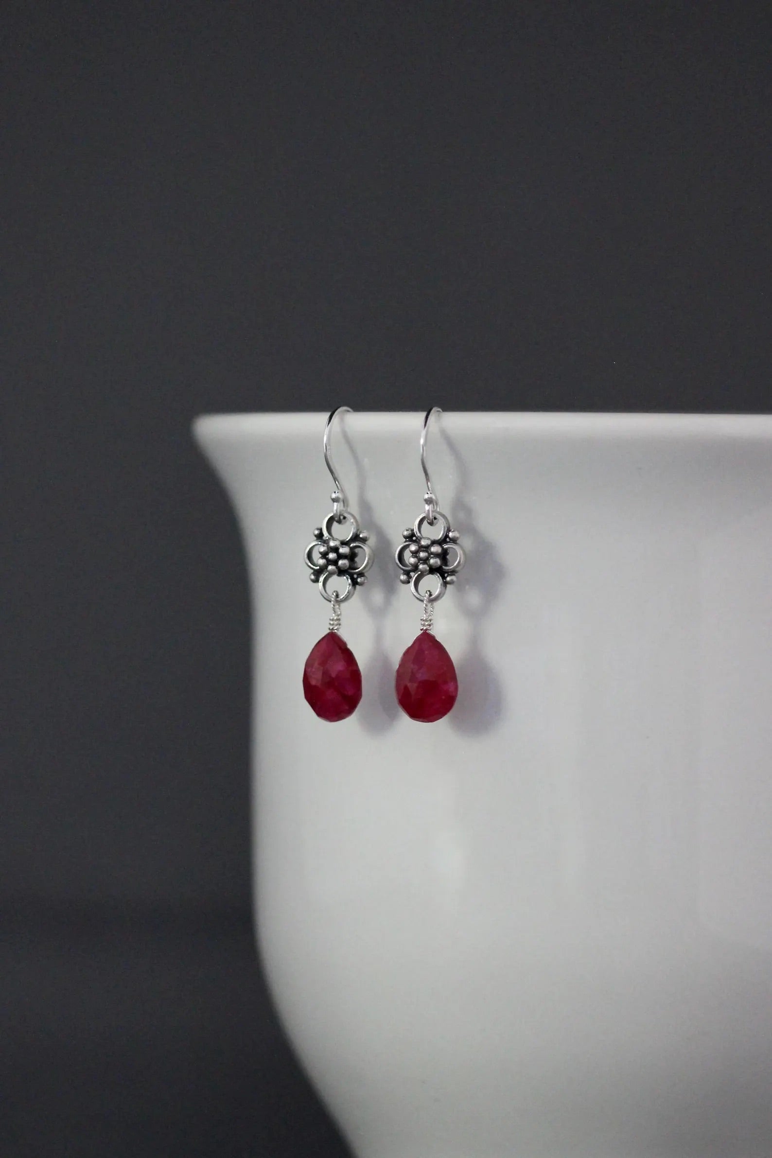 Earrings with teardrop-shaped ruby stones and silver earwires against a gray backdrop