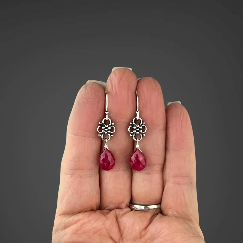 Earrings with teardrop-shaped ruby stones and silver earwires held in the palm of a person's hand