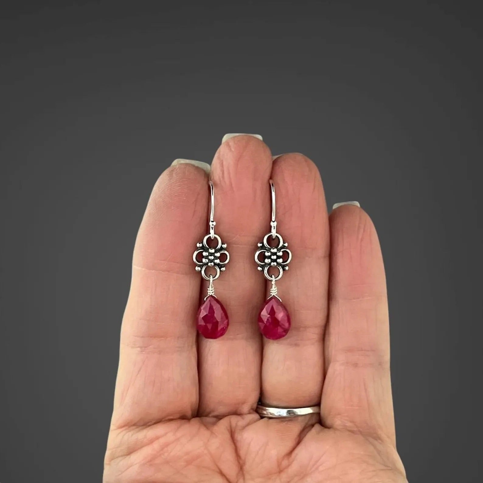 Earrings with teardrop-shaped ruby stones and silver earwires held in the palm of a person's hand
