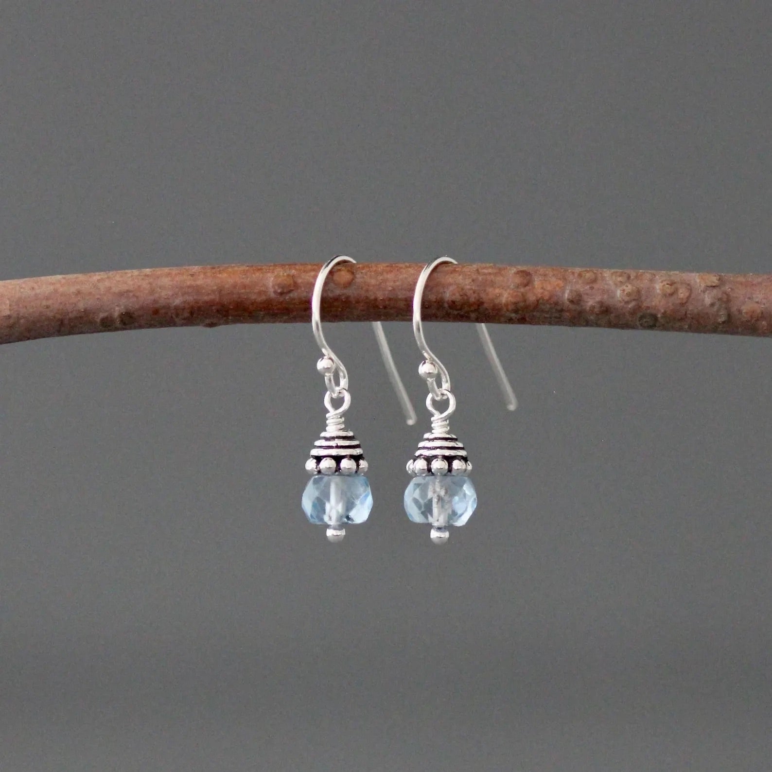 Silver earrings with blue beads hanging on a branch against a gray background