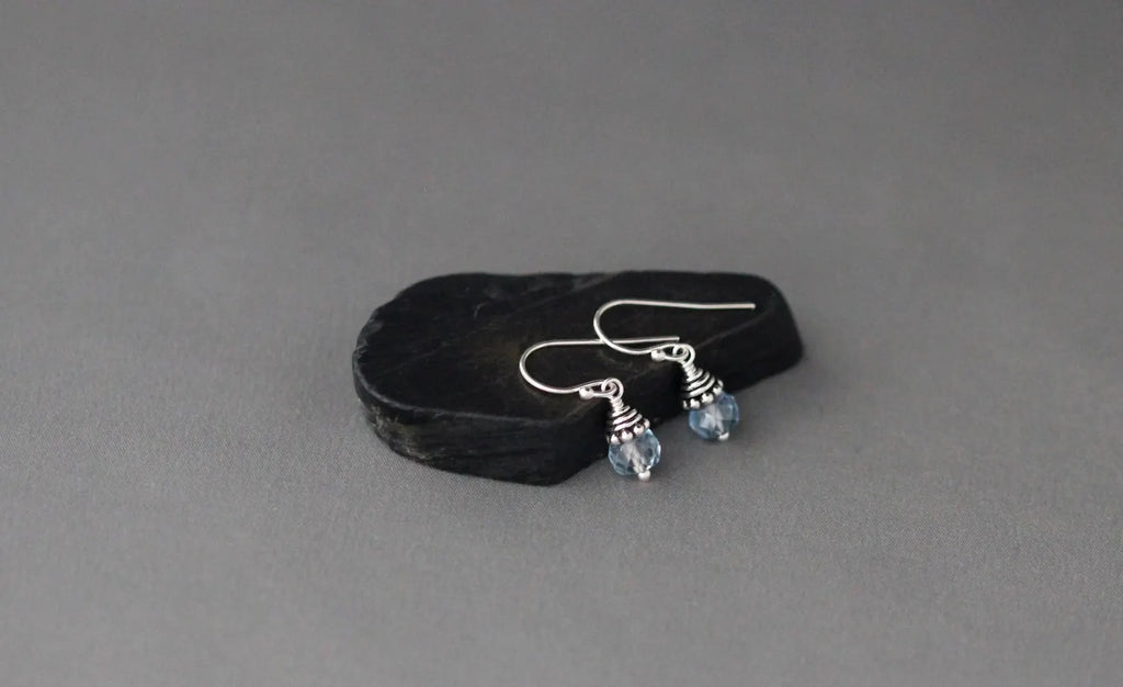 Silver earrings with blue gemstones on a black stone against a gray background