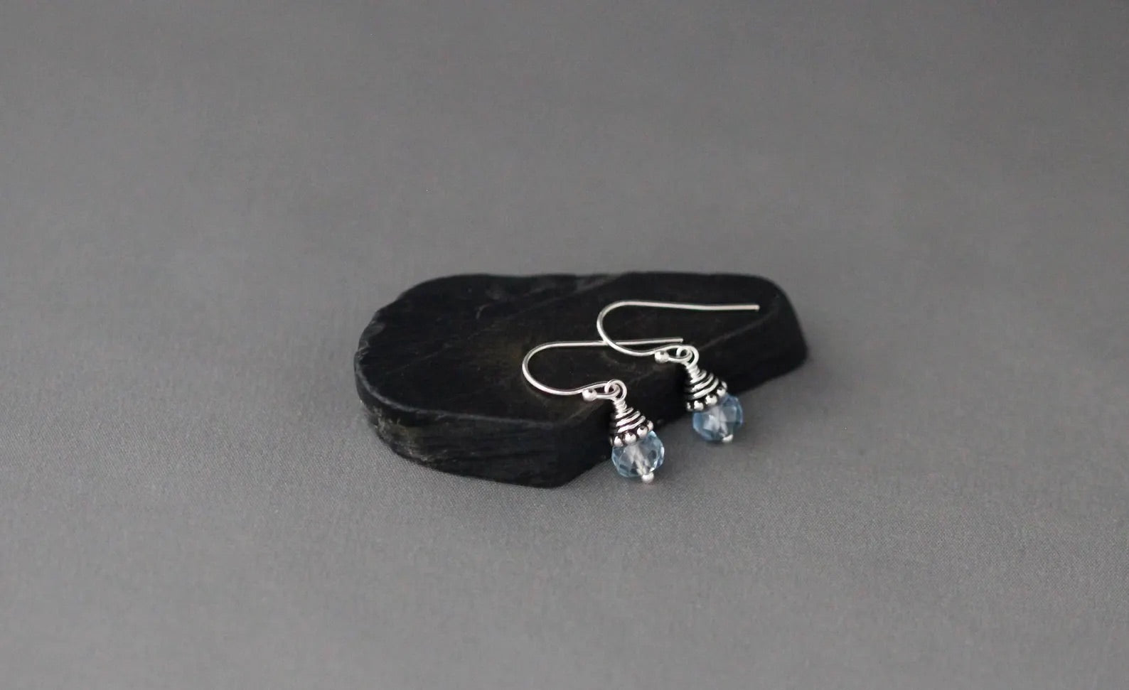 Silver earrings with blue gemstones on a black stone against a gray background