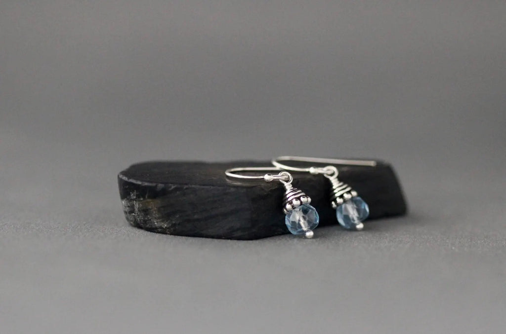Silver earrings with blue beads on a dark stone surface